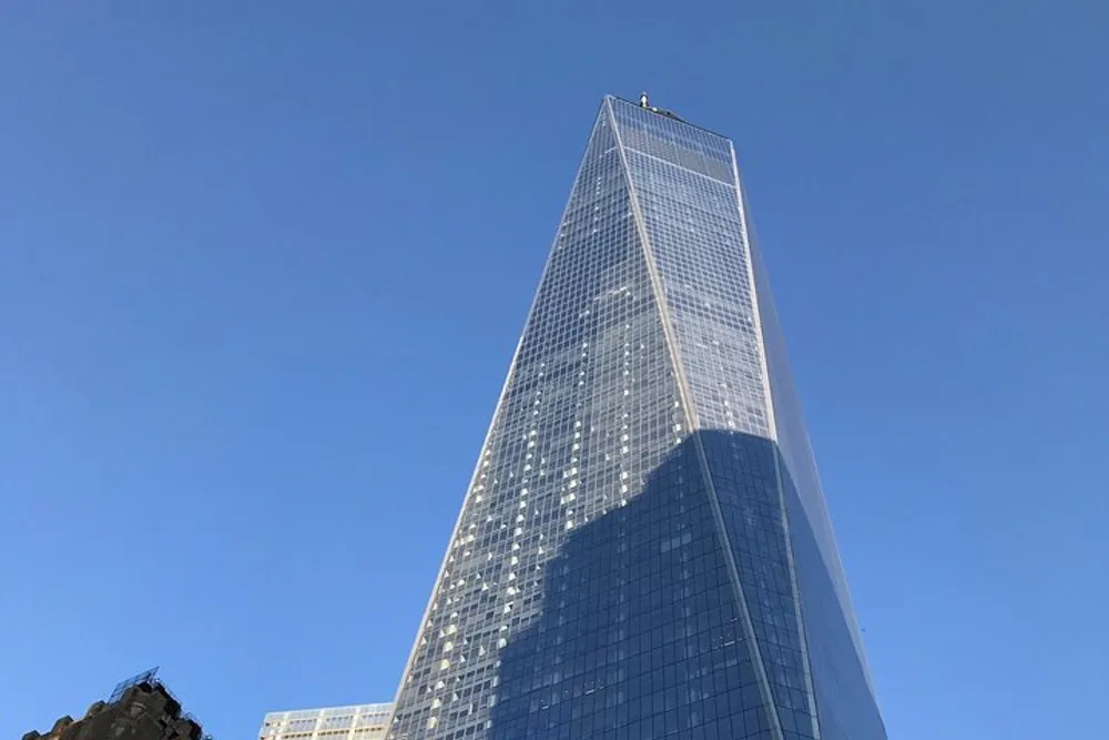 The image shows a tall glass skyscraper towering into a clear blue sky