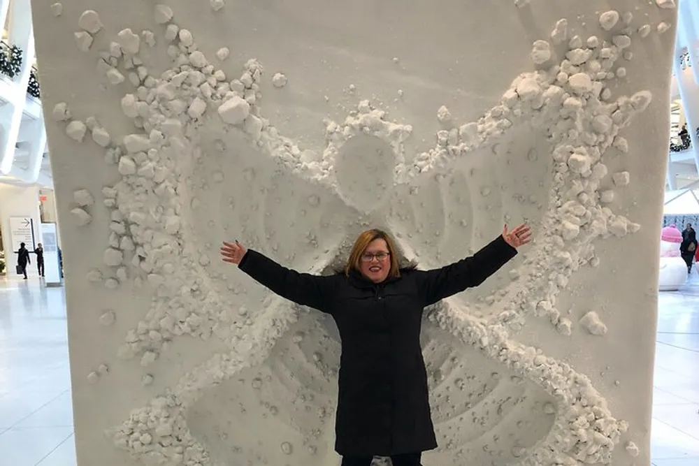 A person is standing in front of a three-dimensional wall with a snow angel impression extending their arms to match the wings of the angel