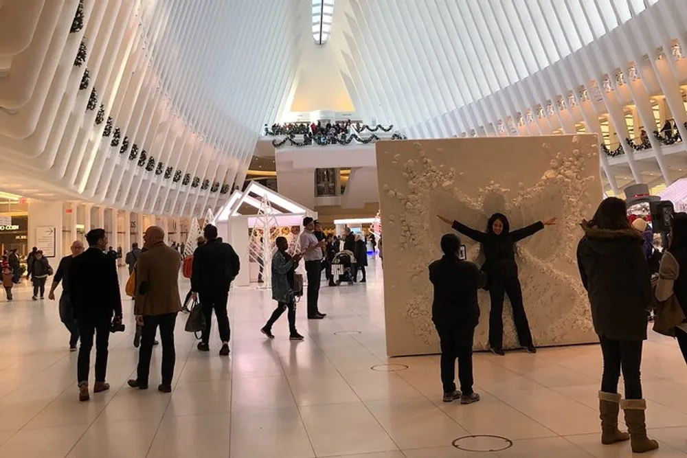 People are walking and interacting with an exhibit inside a modern building with an undulating white ceiling