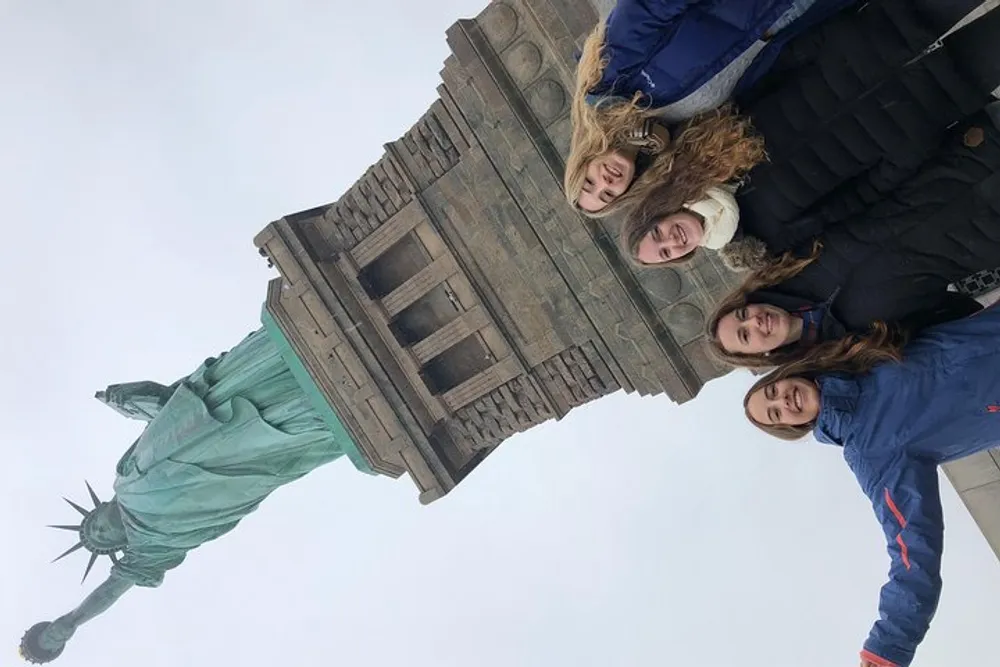 Four individuals are posing for a photo with the Statue of Liberty towering in the background