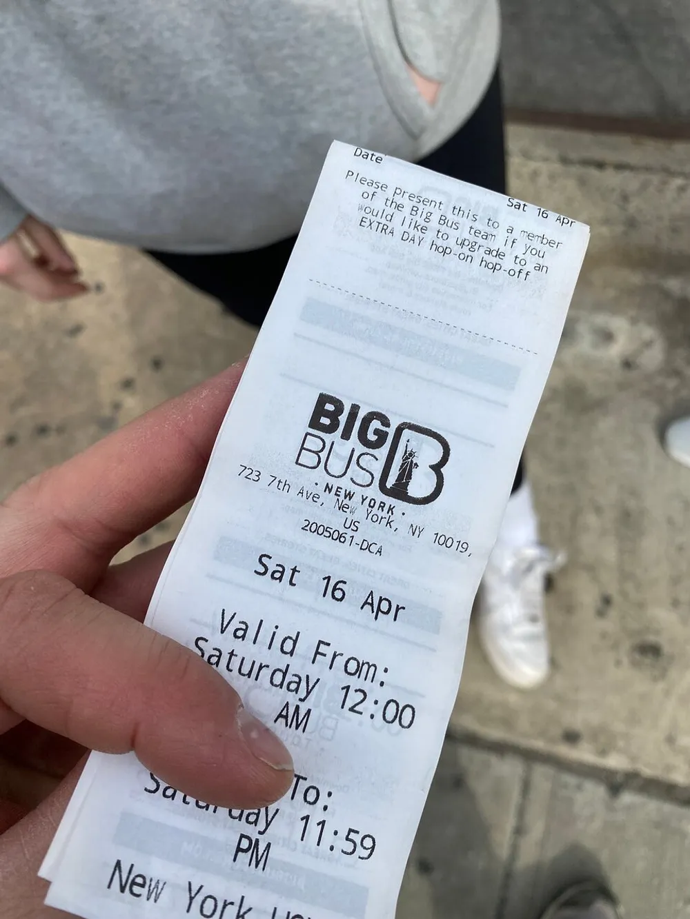 A person is holding a Big Bus New York hop-on hop-off bus tour ticket with the date and valid time period clearly visible