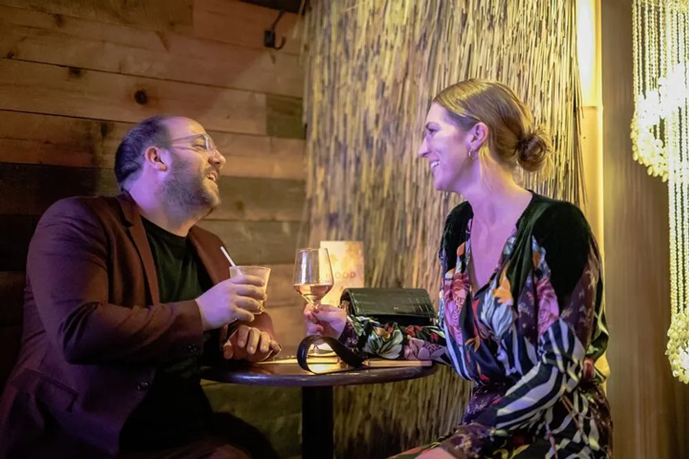 A man and a woman are enjoying a conversation and drinks at a warmly lit cozy table