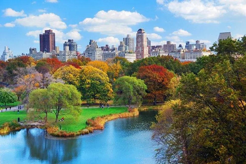 The image showcases a vibrant autumnal view of Central Park with its colorful foliage and tranquil pond against the backdrop of New York Citys skyscrapers