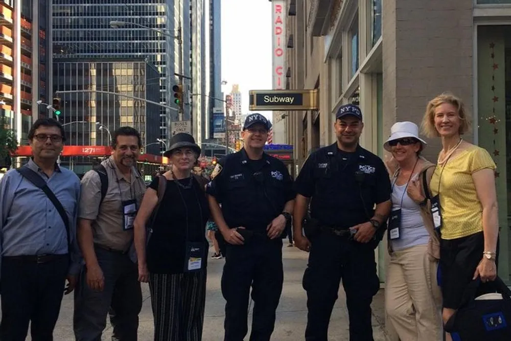 A group of tourists is posing for a photo with two New York City police officers on a sunny day in an urban setting
