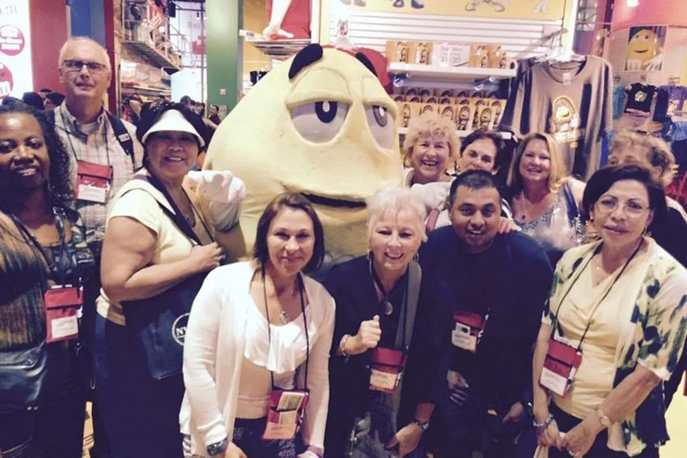 A group of smiling people are posing for a photo with a person in a large cartoonish yellow character costume at what appears to be an event or a themed venue
