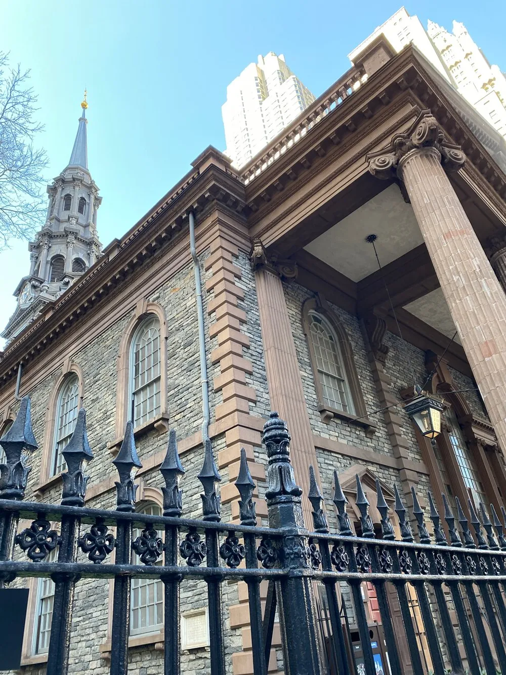 The image shows a historical building with classic architectural details and a wrought iron fence juxtaposed against a modern skyscraper in the background