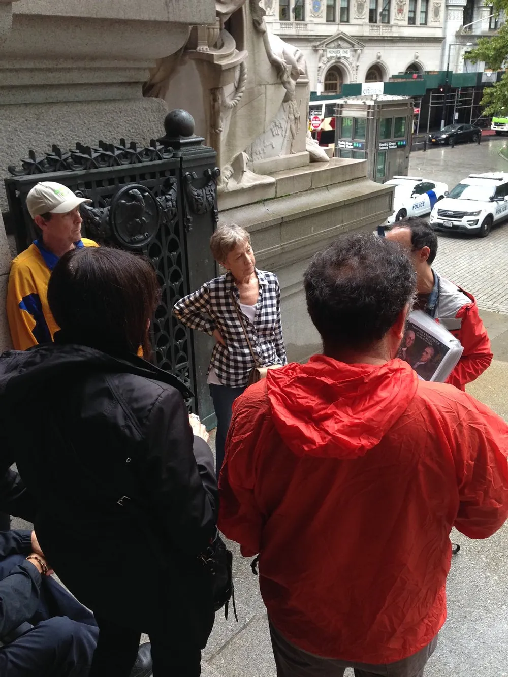 A group of people appears engaged in an outdoor discussion near a historical buildings gate with one person holding what looks to be a magazine or folder