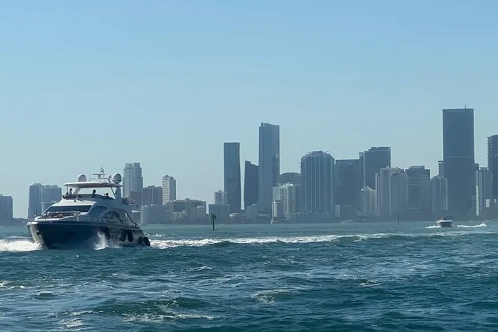 A yacht is cruising in the foreground with a backdrop of a modern skyline viewed from the water