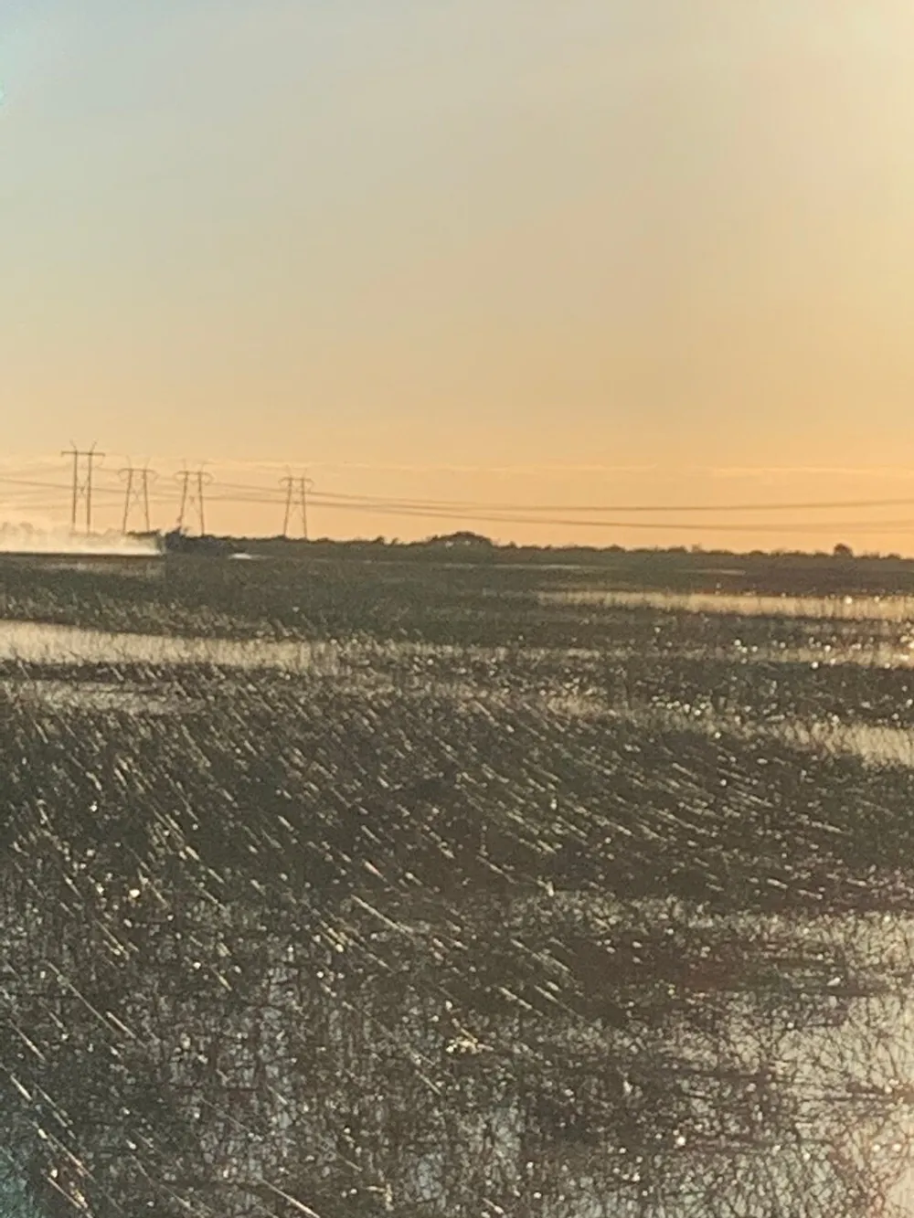 The image captures a serene landscape at dusk with power lines silhouetted against the sky and a field or body of water glistening in the foreground