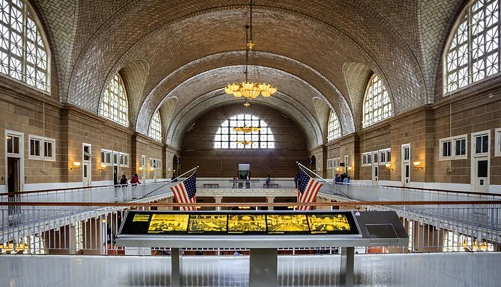 This image shows an expansive interior of a historic building with a vaulted ceiling featuring two American flags and a display case in the foreground