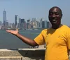 A smiling person is playfully posing as if they are holding the Manhattan skyline in their outstretched hand