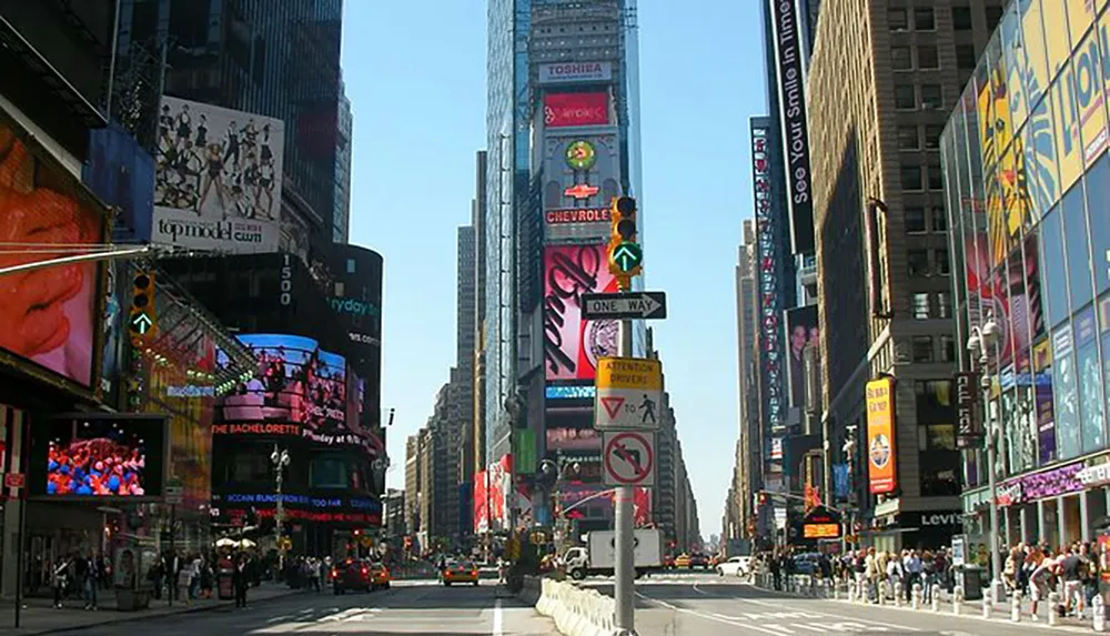 The image shows a bustling Times Square in New York with its iconic electronic billboards and busy streets under a clear blue sky