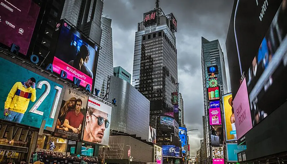 The image captures the bustling atmosphere of Times Square highlighted by its towering buildings adorned with vibrant large-scale advertisements under an overcast sky