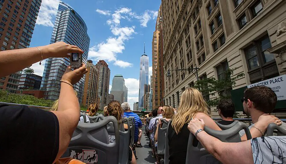 Tourists on an open-top bus tour are seen capturing photos of cityscapes and skyscrapers on a sunny day