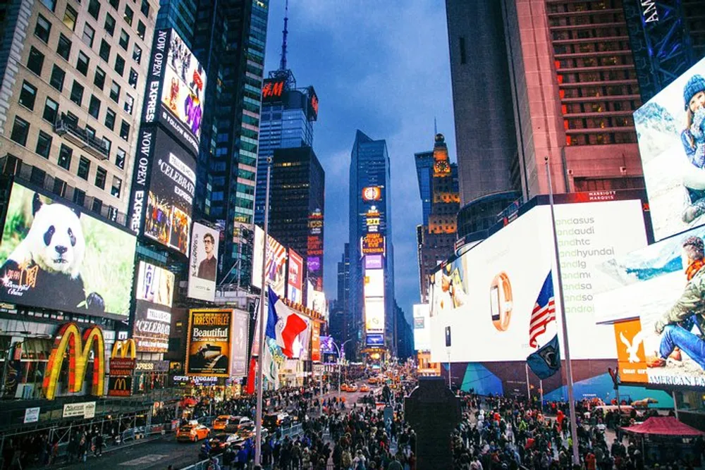 The image shows a bustling Times Square in New York City with bright digital billboards and crowded streets at dusk