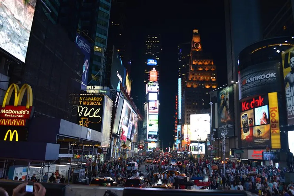 The image shows a bustling Times Square at night illuminated by numerous electronic billboards and crowded with people and vehicles