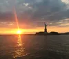 The sun sets beautifully behind the Statue of Liberty casting a warm glow over the water