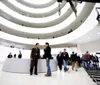 The image shows the interior of a museum with a spiral walkway where numerous visitors are either walking around or engaged in conversation