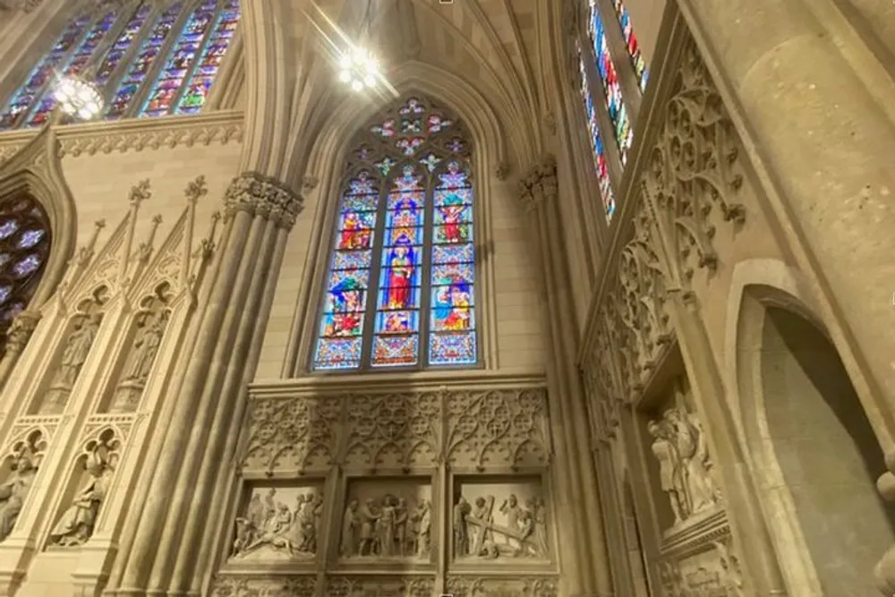 The image shows the interior of a Gothic cathedral with a large stained glass window and ornate stone carvings