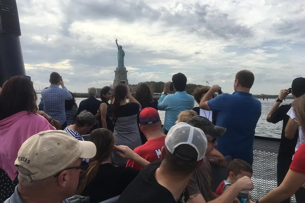 A group of tourists on a boat are taking photos of the Statue of Liberty