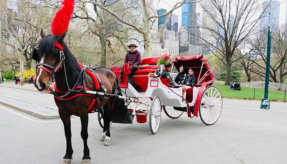 A horse-drawn carriage with a driver and passengers on board travels through a park-like setting with skyscrapers in the background