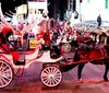 A horse-drawn carriage is navigating through a bustling Times Square lit by colorful billboards and signs at dusk