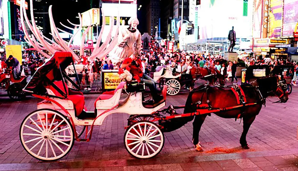 A horse-drawn carriage waits amidst the bustling lights and crowds of Times Square at night