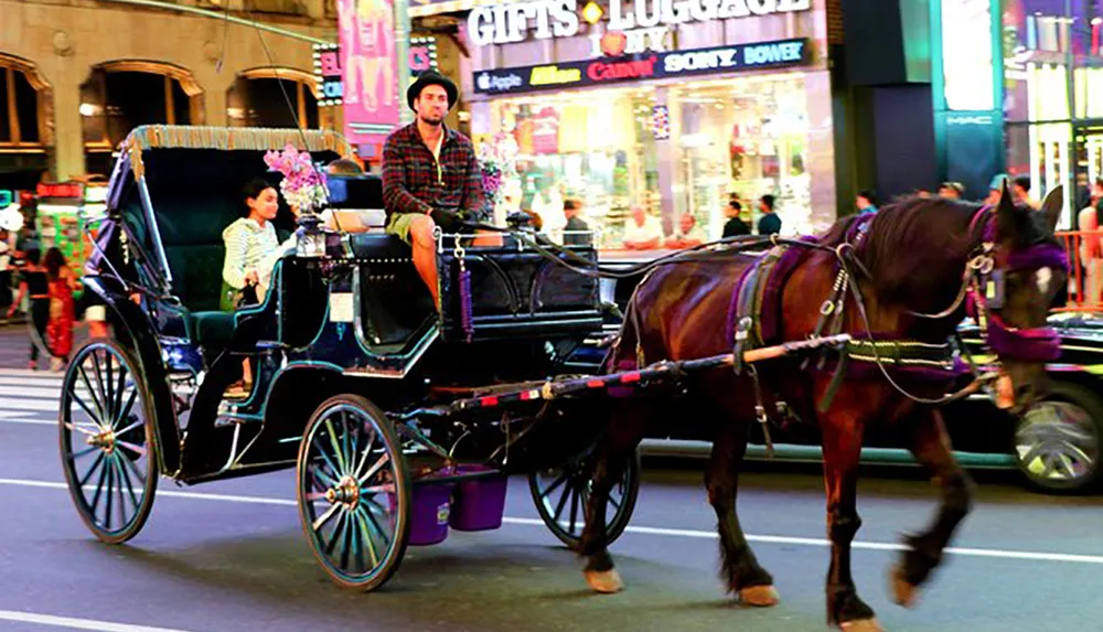 A horse-drawn carriage navigates through a brightly-lit urban street with a driver and a passenger on board