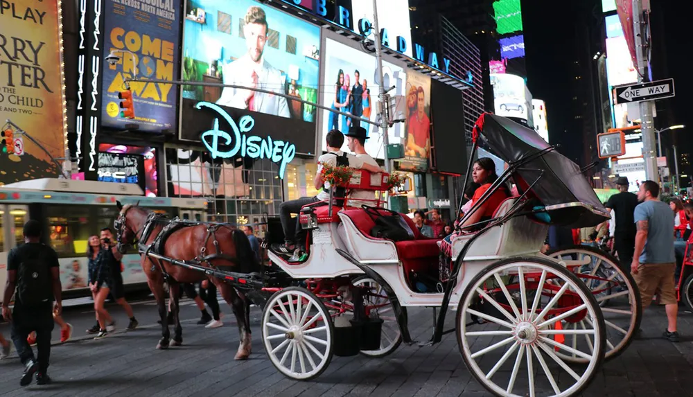 A horse-drawn carriage is navigating through a bustling Times Square lit by colorful billboards and signs at dusk