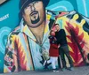 A couple is posing in front of a vibrant mural of a legendary singer