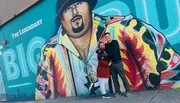 A couple is posing in front of a vibrant mural of a legendary singer.