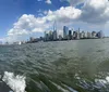 The image is a panoramic view of the Manhattan skyline as seen from a boat on the water featuring clear skies and a few clouds above