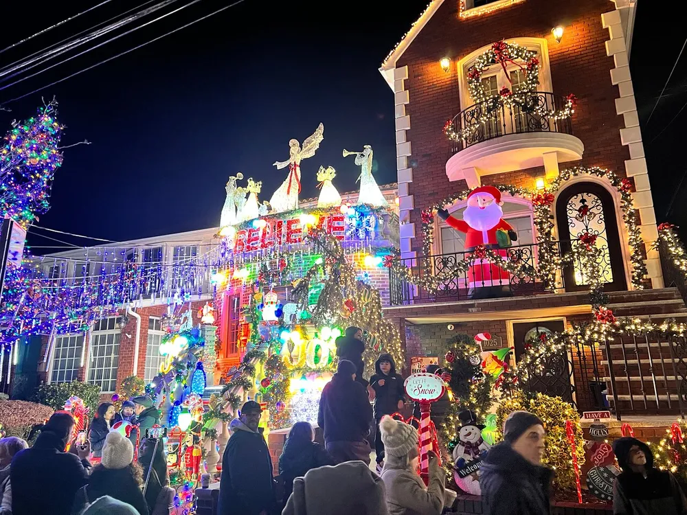 A house is extravagantly decorated with vibrant Christmas lights and decorations drawing the attention of a crowd gathered to admire the festive display