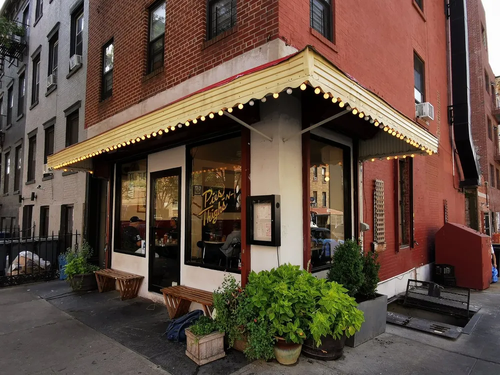 The image shows a cozy corner street caf with an inviting awning lit by a warm glow and patrons visible through the large windows enhancing the urban charm