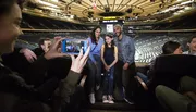 A person is taking a photo of two adults and a child smiling at the camera while sitting in an empty sports arena.