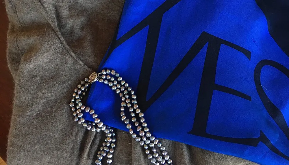 This image depicts a gray sweatshirt partially covered by a blue fabric with white text alongside a strand of metallic beads