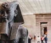 A group of people are posing and smiling for a photo between two ancient Egyptian statues at a museum