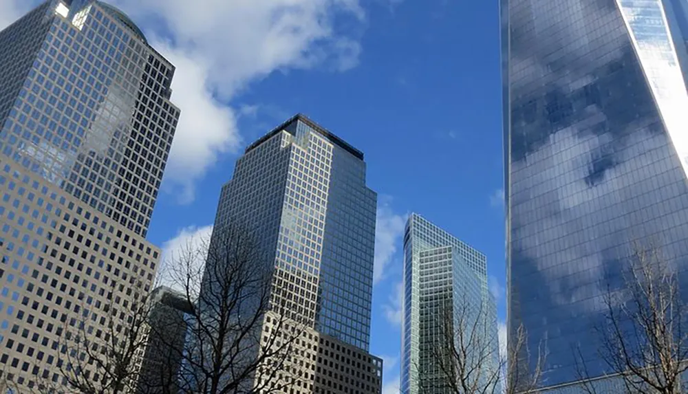 The image showcases a cluster of modern skyscrapers reaching towards a partly cloudy sky reflecting the suns light on their glass facades