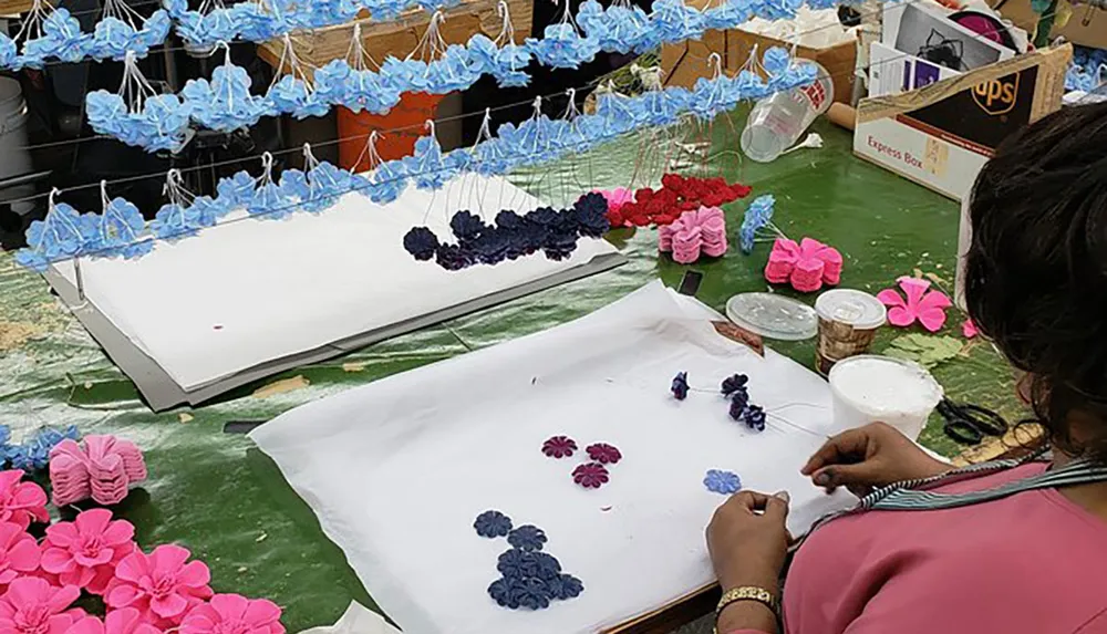 A person is crafting artificial flowers at a workshop filled with colorful flower components and materials