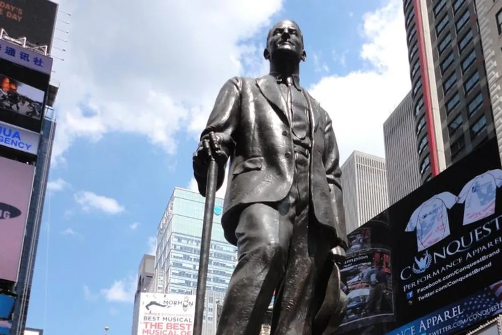 The image shows a statue of a man standing upright with a walking stick set against an urban background of billboards and buildings under a blue sky
