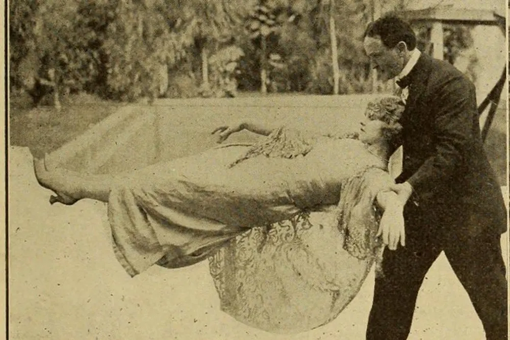 A man in a suit appears to be carrying a woman in a long dress who is lying across his arms in a classic bridal carry pose