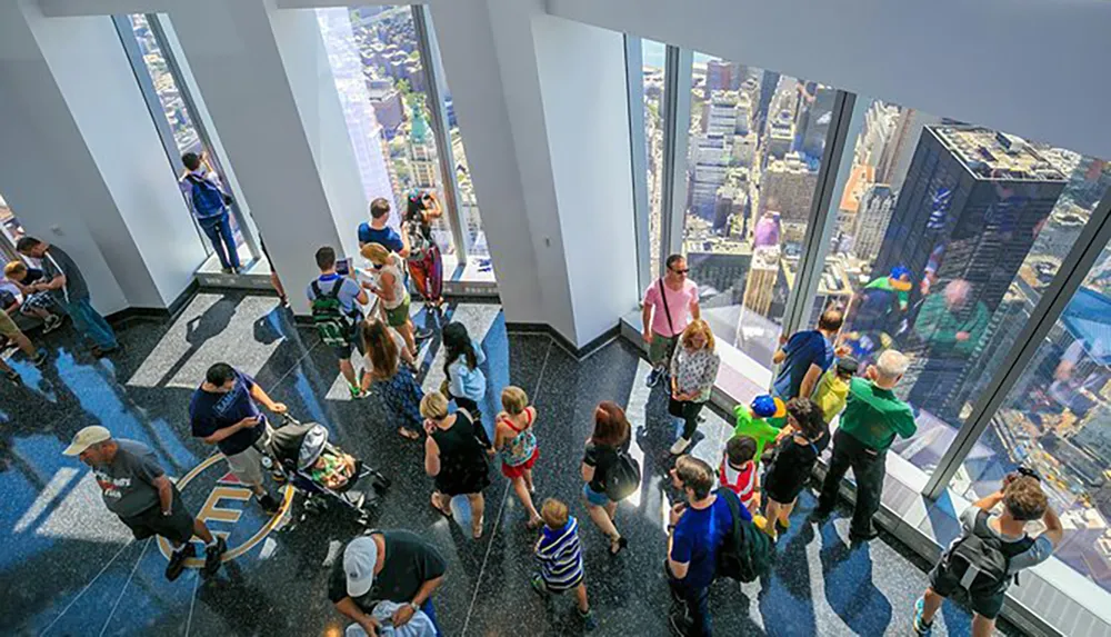 Visitors are enjoying the view from a high vantage point inside a modern observation deck with expansive windows overlooking a cityscape