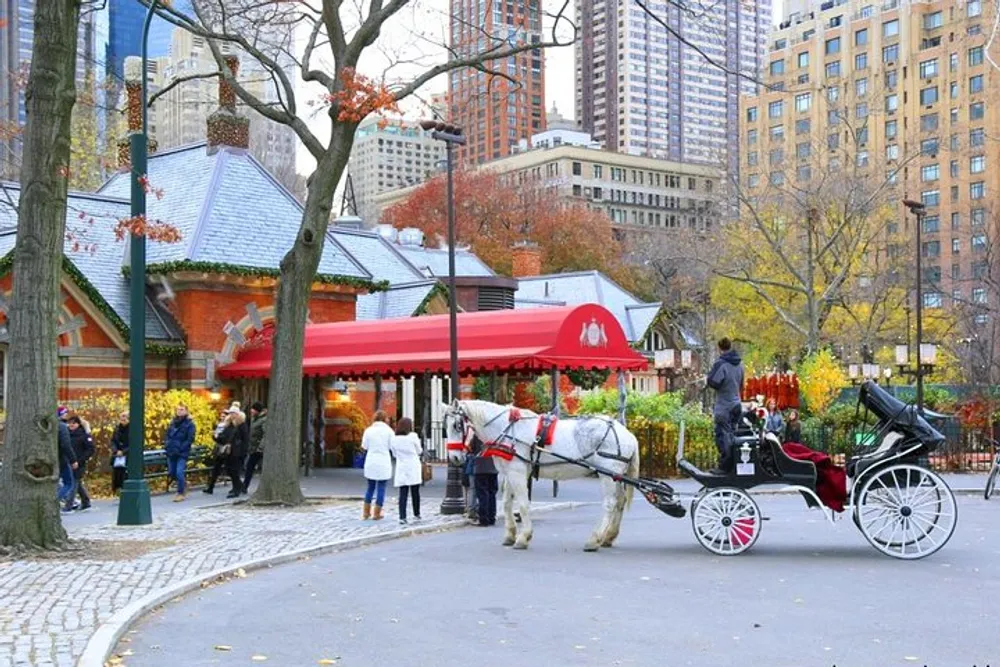 A horse-drawn carriage awaits passengers near a bustling city park cafe surrounded by autumn foliage and urban high-rises