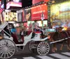 A horse-drawn carriage adorned with yellow and pink plumes and decorations is trotting through an urban street with passengers and a driver onboard amidst modern vehicular traffic