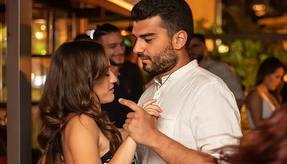 A couple is enjoying an intimate moment on a dance floor locked in a gaze with the man holding the womans hand to his chest