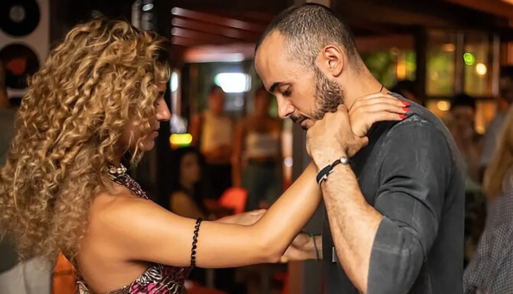 A man and a woman are engaging in a close dance in a social setting possibly a salsa or similar dance style