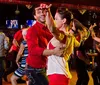 A group of people are joyfully engaging in social dancing at a vibrant venue with a couple in the foreground performing a dance move with eye contact and smiles