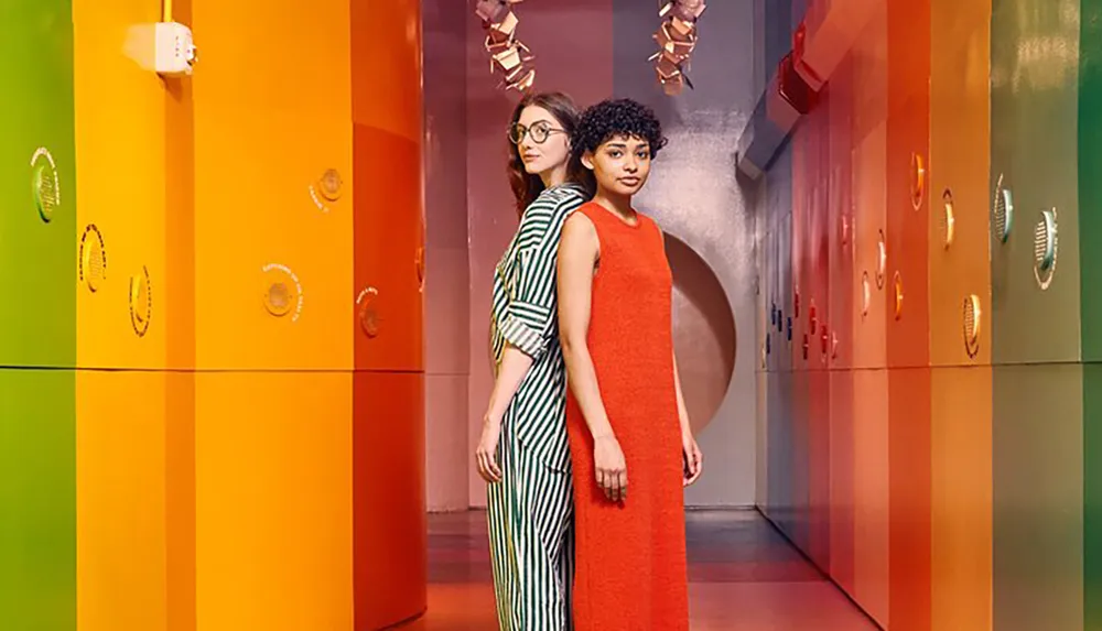 Two people stand back-to-back in a colorful hallway with vibrant geometric patterns and circular wall decorations