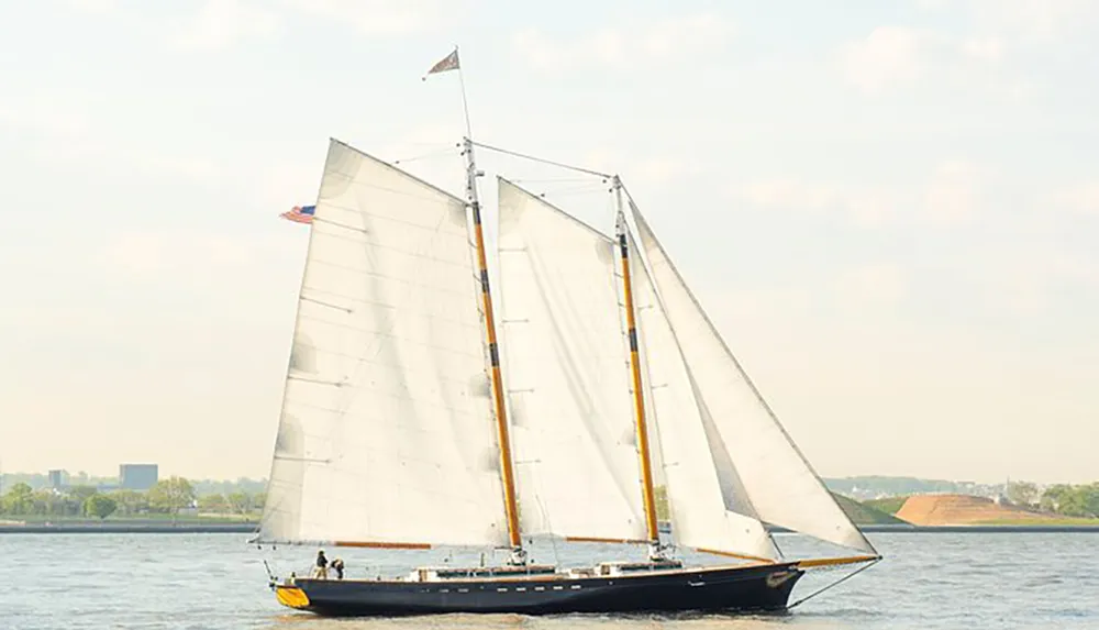 A large sailboat with its sails fully deployed is navigating through the water on a day with clear skies