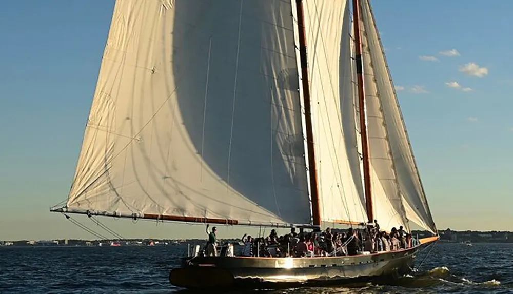 A large sailboat is gliding over the water filled with passengers enjoying a sunny day at sea